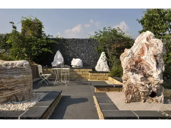 Naturalny monolit kamienny jako rzeźba ogrodowa przy tarasie z czarnego wapienia